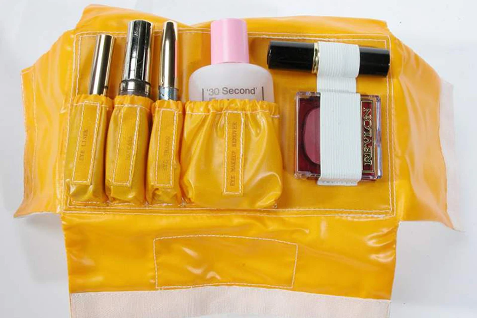 В сумочке ярко желтого цвета уложены румяна, средство для снятия макияжа, губная помада, подводка для глаз и туш для ресниц