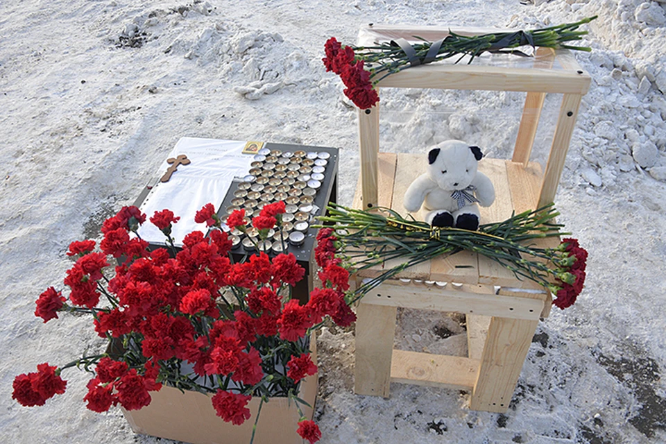 Жители села устроили стихийный мемориал. На столе горят свечи, лежат игрушки и много-много кроваво-красных гвоздик