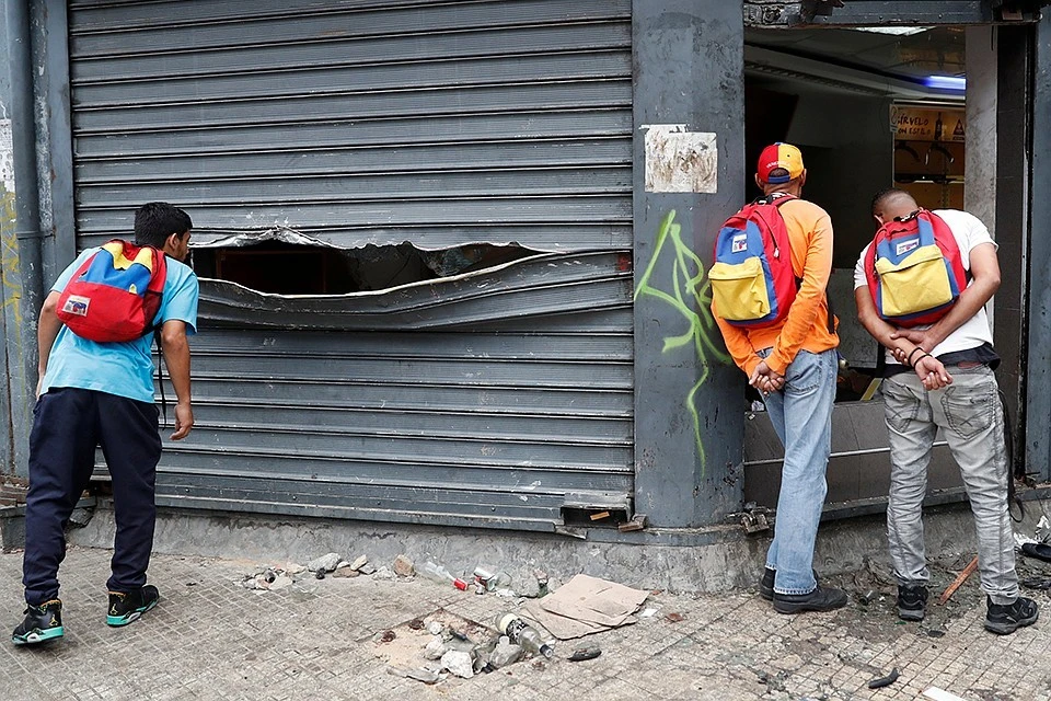 Жители Каракаса рассматривают разгромленный в ходе беспорядков магазин по продаже спиртного.
