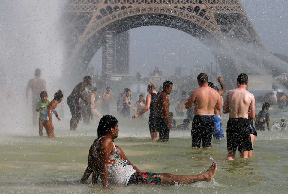 Туристы охлаждаются в фонтанах у подножия Эйфелевой башни в Париже.