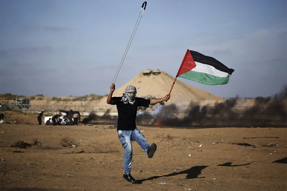 Палестинец выпускает камень из пращи в сторону израильских солдат.