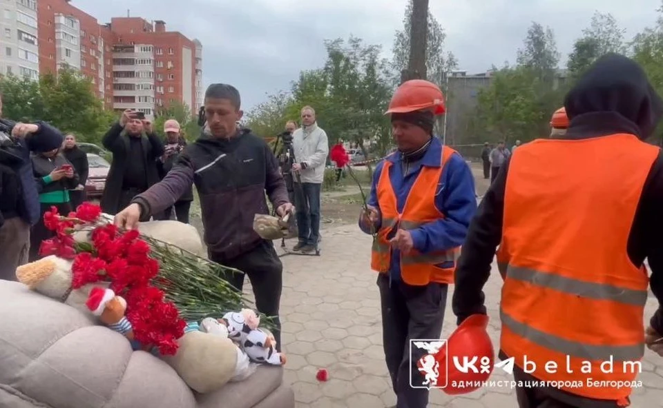 Жители и рабочие несут цветы и игрушки к стихийному мемориалу у пострадавшего дома в Белгороде.