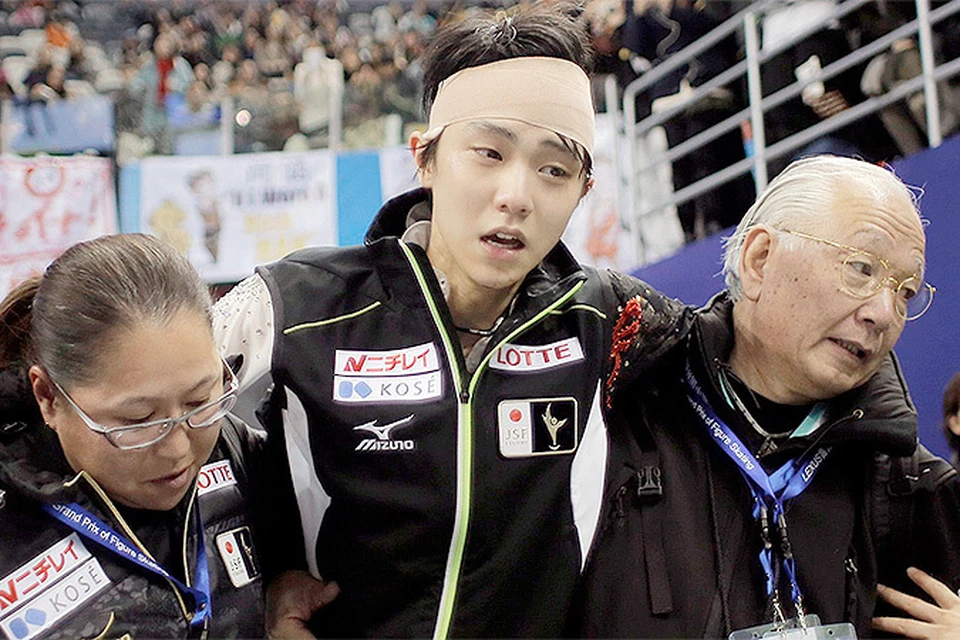 Тренеры помогают японцу Ханю уйти в подтрибунное помещение после оглашения оценок спортсмена